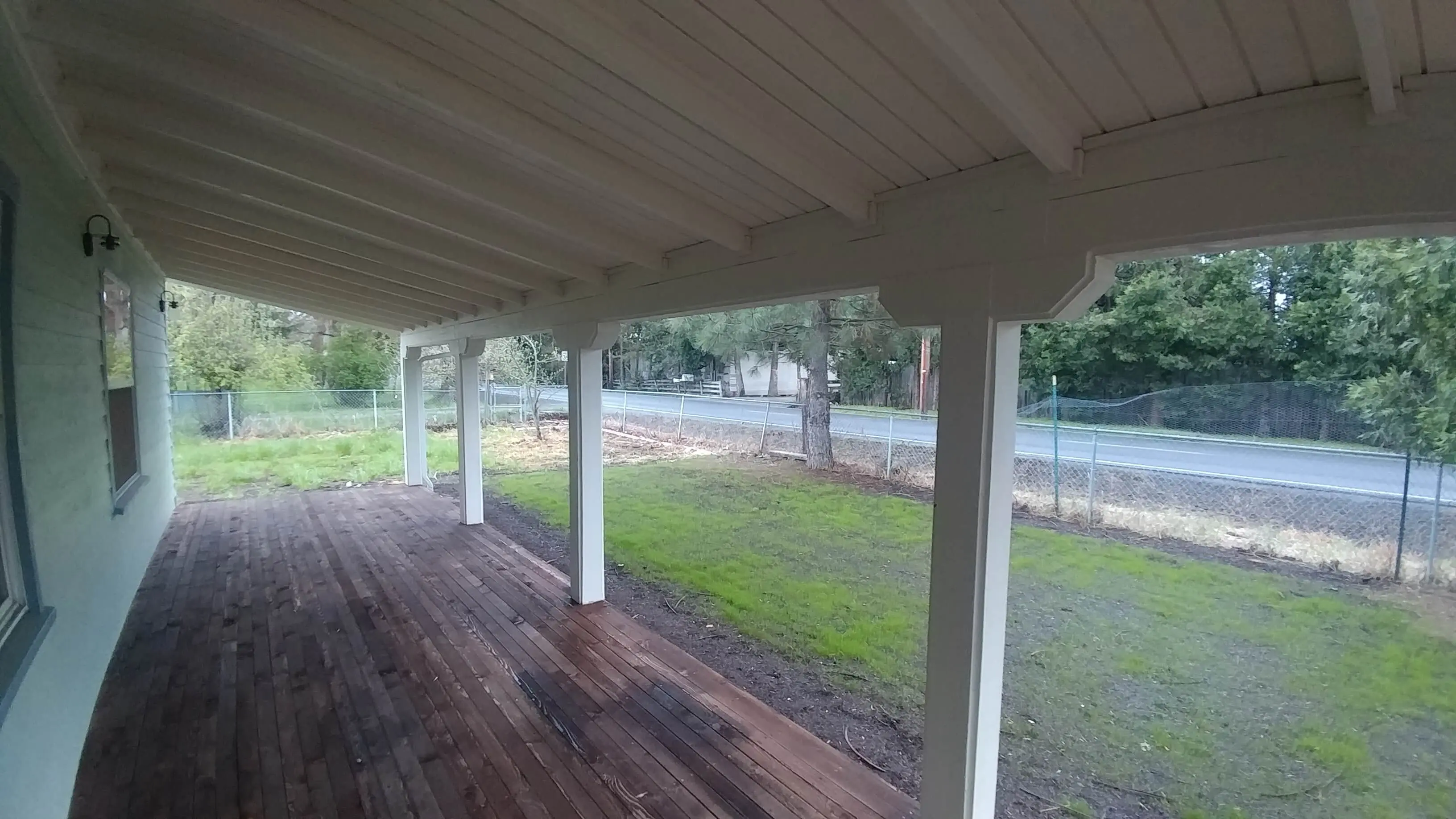 Covered porch overlooking grassy yard and road.