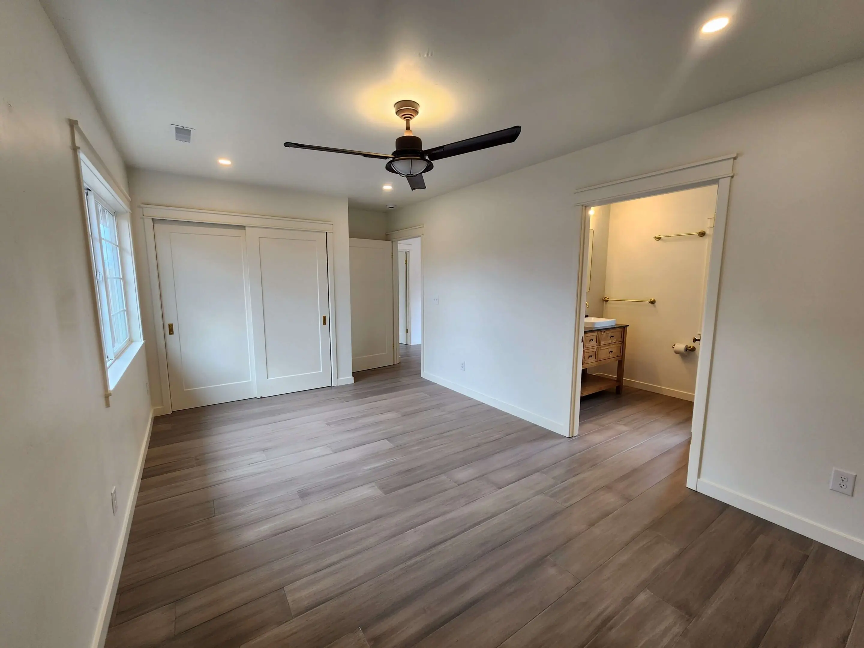 Empty room with wooden floor and fan.