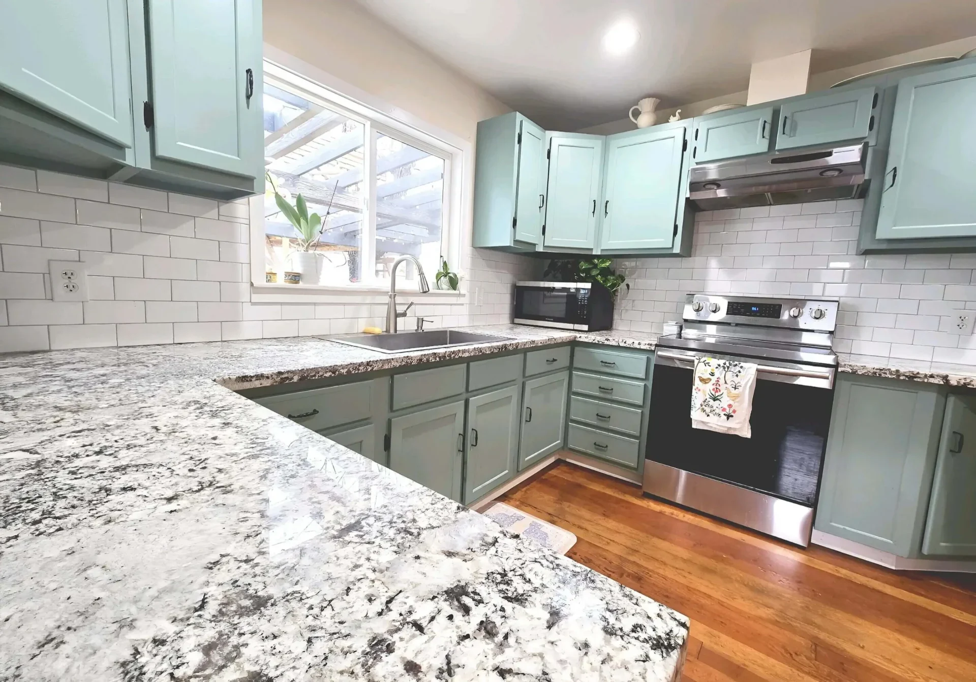 Modern kitchen with green cabinets, granite countertops, and hardwood floors.
